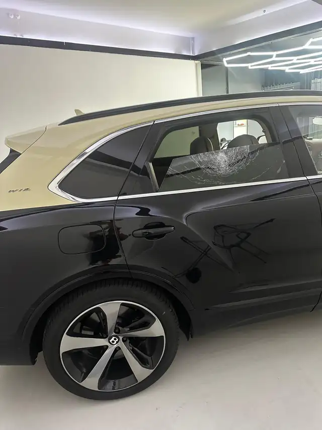 Black and cream Bentley Bentayga inside a garage in Enfield with a smashed rear door window
