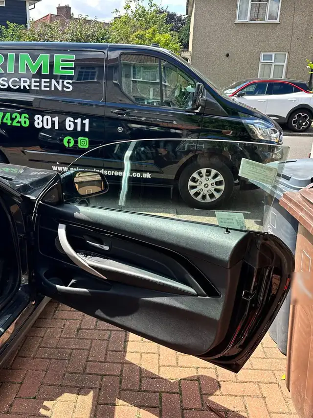 Black BMW 4 Series coupe on a front drive in Enfield with a new frameless door window fitted, the Prime Windscreens van outside