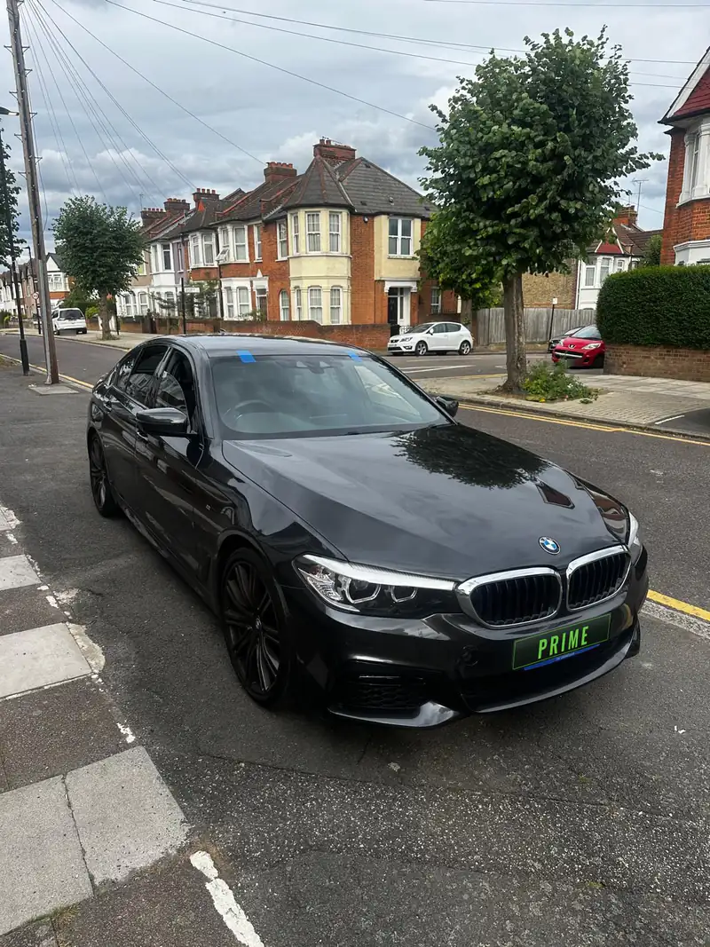Black BMW 5 Series on a street corner in Cricklewood with blue tape on its new windscreen
