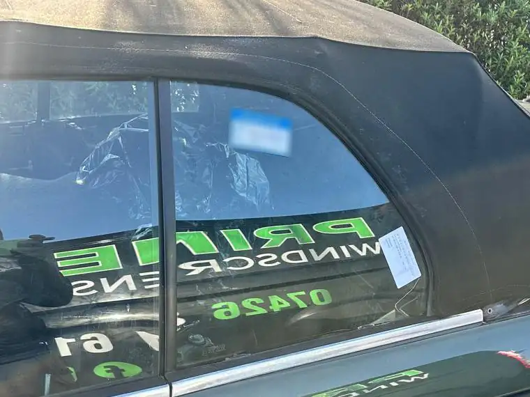 New rear quarter window on a dark green classic BMW 3 Series convertible, with the Prime Windscreens van reflected in the glass