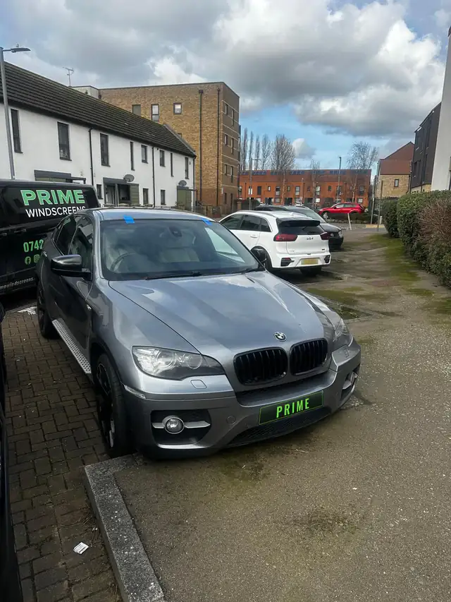 Grey BMW X6 in a residential car park after a mobile windscreen replacement, with blue tape on the new glass