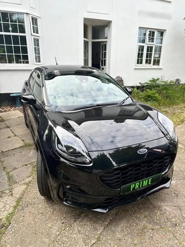 Black Ford Puma on a front drive with two strips of tape holding its new windscreen while the adhesive sets