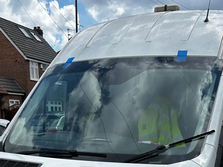 White Ford Transit high roof van on a residential street with blue tape holding its new windscreen at the top edge