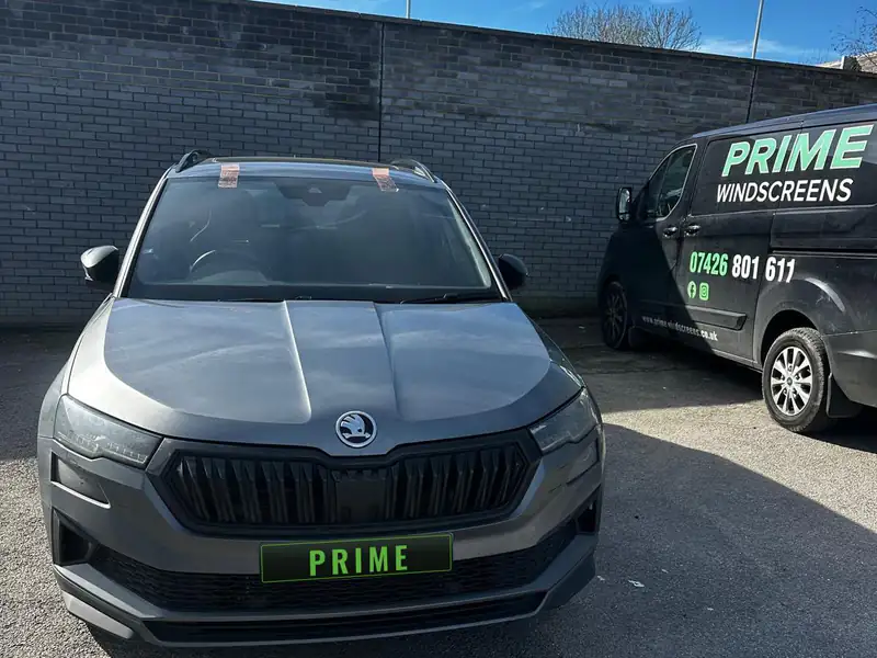 Grey Skoda Kamiq in a walled car park with tape holding its new windscreen, the Prime Windscreens van parked alongside