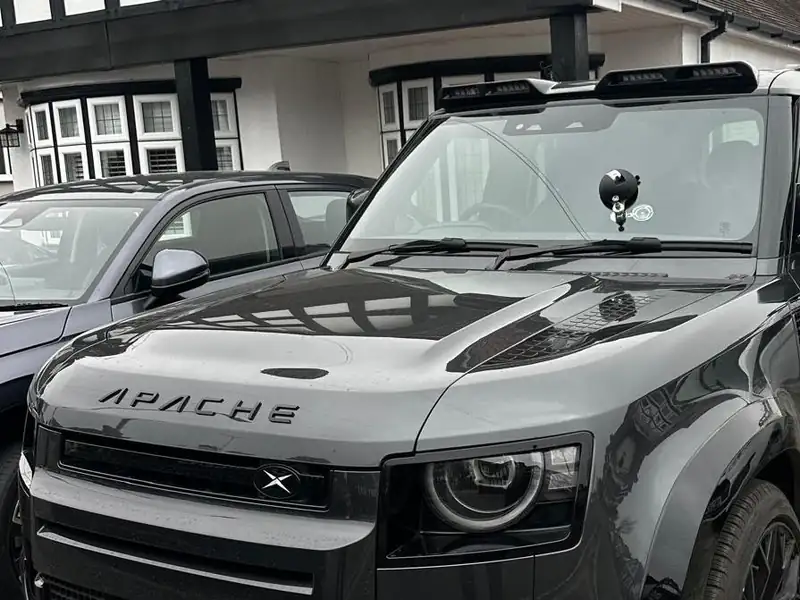 Dark grey Land Rover Defender on a block paved drive, with a chip repair bridge and resin injector fixed low on its windscreen