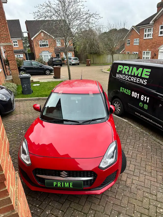 Red Suzuki Swift on a block paved drive in Edgware with a new windscreen, next to the Prime Windscreens van