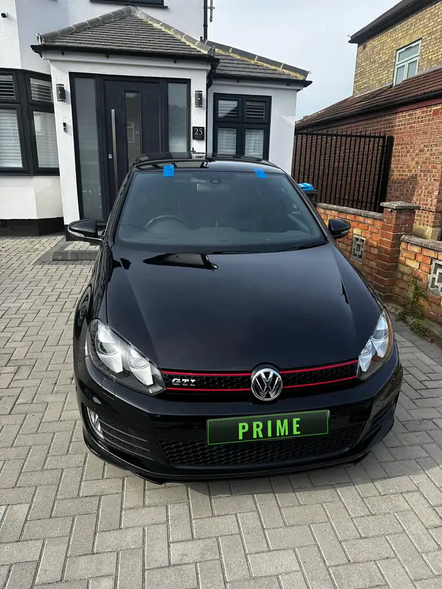 Black Volkswagen Golf GTI on a driveway with its replacement windscreen taped in place while the bond cures