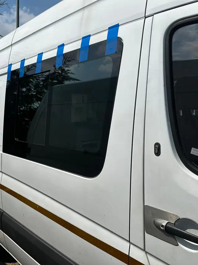 White welfare van with a new side window, held along its top edge by strips of blue tape